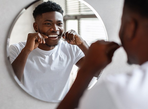 Man smiling while flossing in bathroom mirror